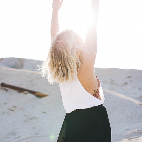 Femme blonde en plein désert qui lève les mains vers le ciel