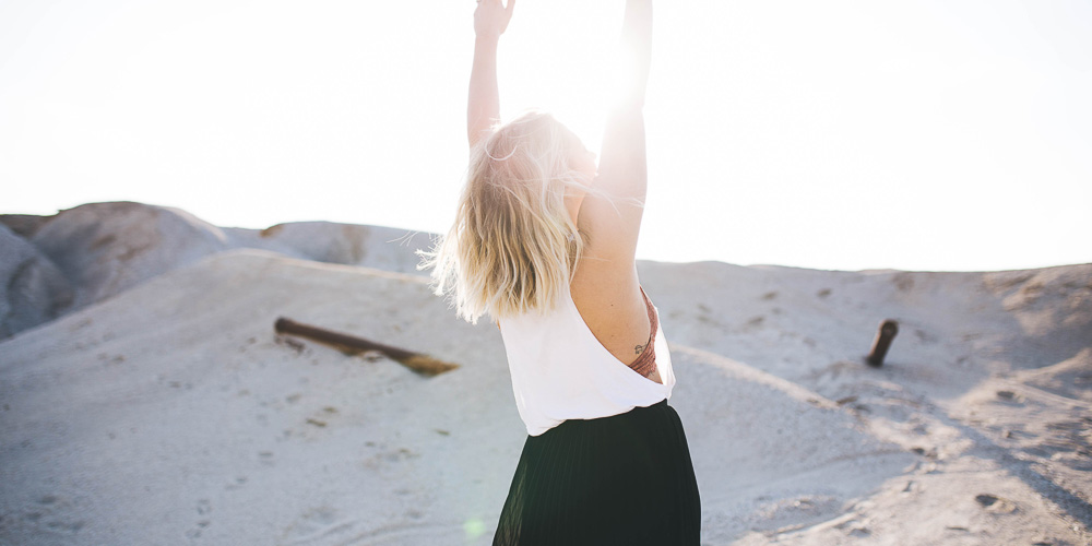 Femme blonde en plein désert qui lève les mains vers le ciel